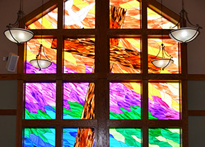 Chapel with a large, colorful stained-glass window and hanging light fixtures at Milaca Elim Meadows