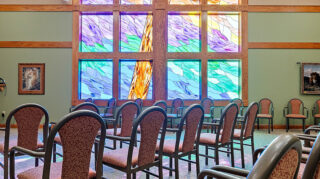 Chapel space with rows of chairs facing a large stained glass window with wood framing and hanging light fixtures at Milaca Elim Meadows
