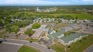 Aerial view of Milaca Elim Meadows showing multiple residential buildings, parking areas, surrounding roads, trees, and open landscape