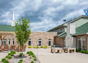 Landscaped courtyard with walking paths, patio seating, trees, and surrounding building spaces at Milaca Elim Meadows