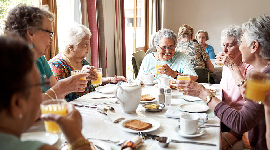 Group of older adults seated together at a table enjoying a meal with coffee and juice in a dining setting, representing social dining and community connection like at Milaca Elim Meadows