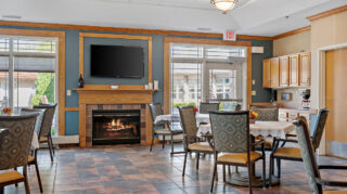 Dining and bistro-style seating area with tables, chairs, fireplace, wall-mounted television, and kitchenette cabinetry at Milaca Elim Meadows