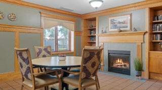 Small seating area with a round table, upholstered chairs, built-in shelving, and a fireplace with wood framing and tile surround at Milaca Elim Meadows