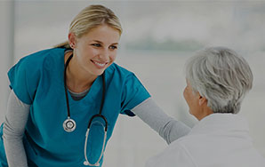 Healthcare worker leaning toward an older adult during a supportive interaction in a bright indoor setting, representing compassionate hospice care like at Milaca Elim Meadows