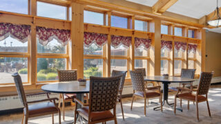 Dining seating area with round tables, chairs, and large windows allowing natural light and outdoor views at Milaca Elim Meadows
