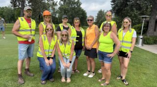 Adults in bright safety vests pose together on the course during the 2026 Milaca Elim Meadows Golf Classic at Stones Throw Golf Course.