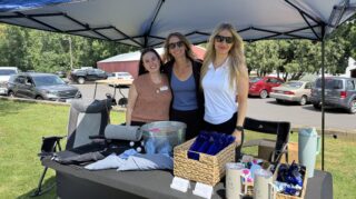 Three sponsor representatives stand behind a promotional table under a canopy during the 2026 Milaca Elim Meadows Golf Classic at Stones Throw Golf Course.