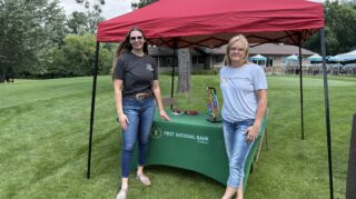 Two adults stand at a First National Bank of Milaca sponsor tent during the 2026 Milaca Elim Meadows Golf Classic at Stones Throw Golf Course.